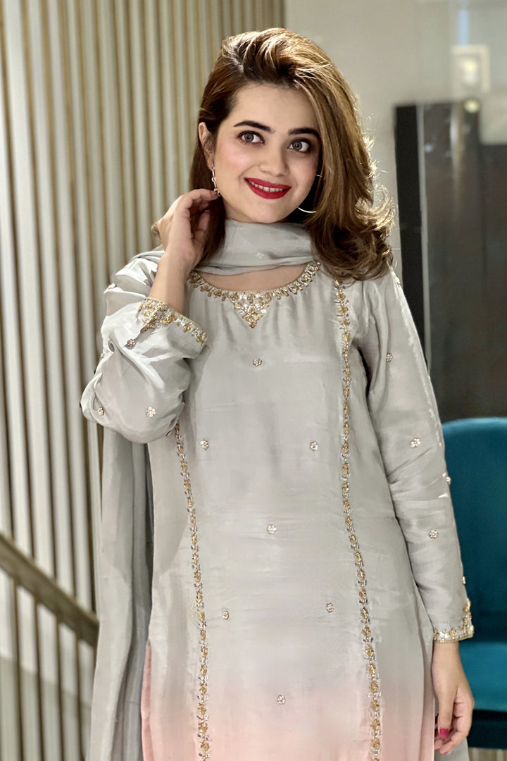 Woman wearing a light gray traditional outfit with gold embroidery indoors.