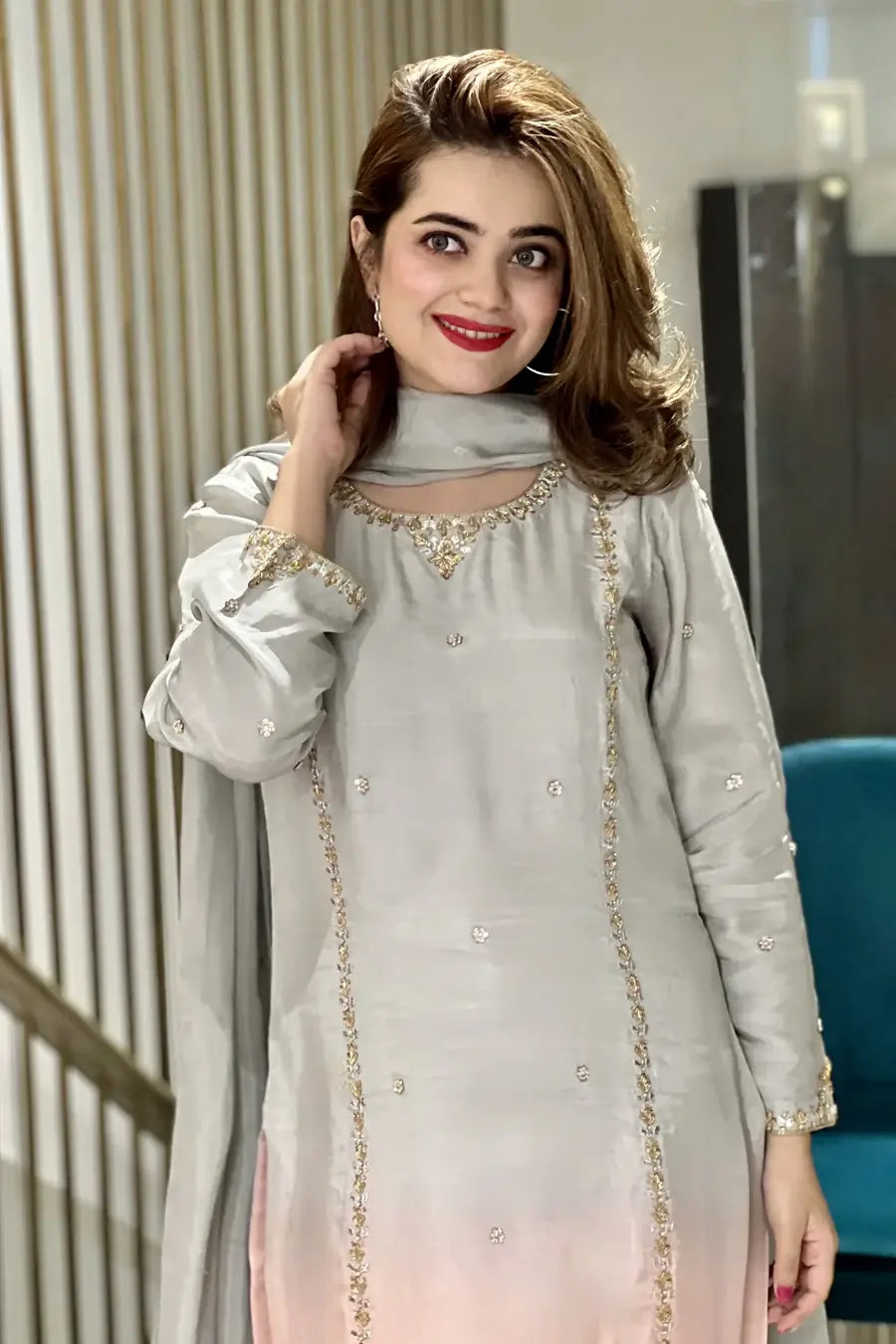 Woman wearing a light gray traditional outfit with gold embroidery indoors.