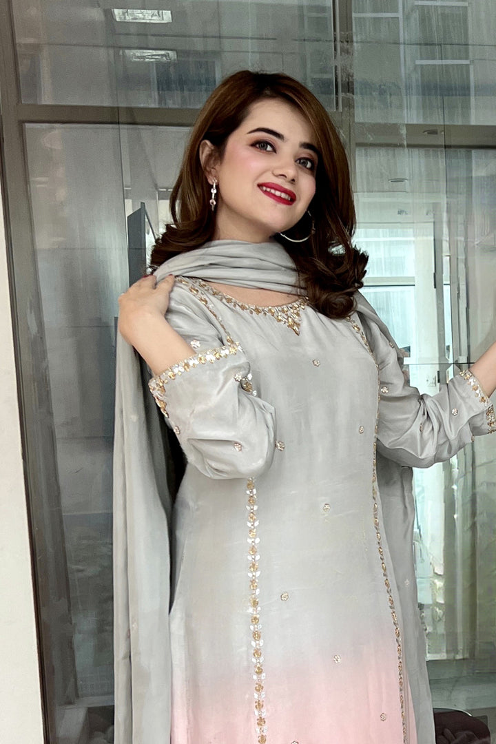 Woman in a light gray traditional outfit with a matching dupatta, standing indoors.