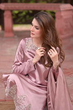 Woman in a pink traditional outfit with intricate designs sitting outdoors.
