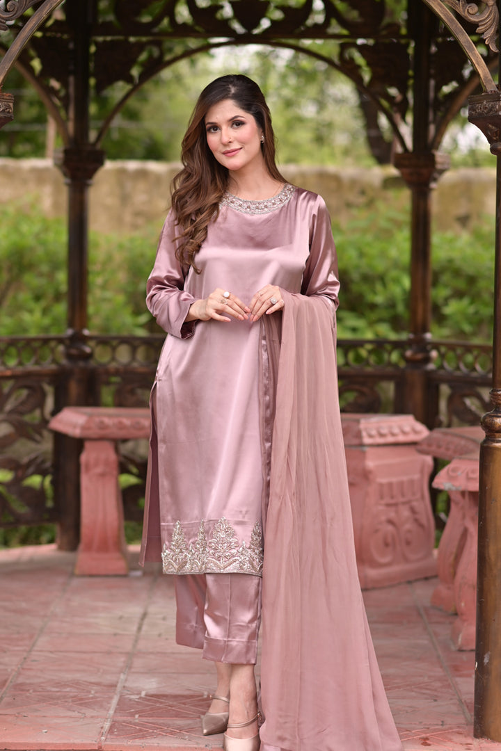 Woman in a pink traditional outfit standing outdoors with greenery in the background