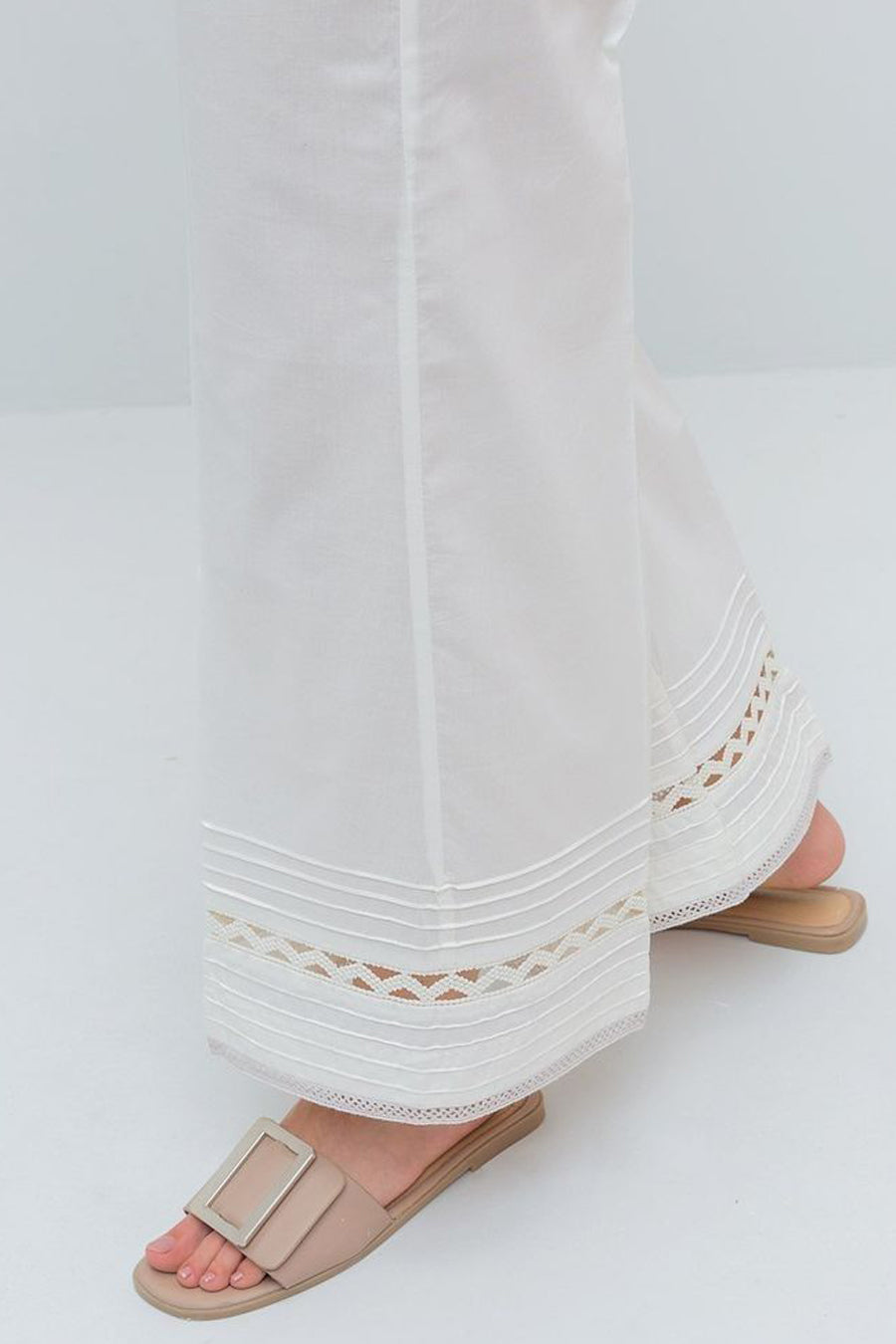 White pants with lace detailing and beige sandals on a white background