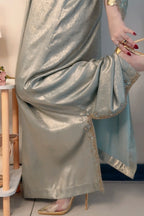 Person wearing a silver saree with gold border indoors