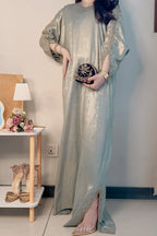 Woman in a long, light-colored dress holding a clutch in a room with a table and shoes.