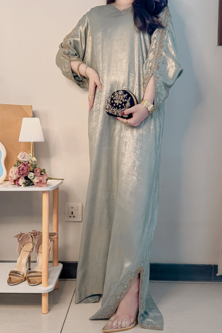 Woman in a long, light-colored dress holding a clutch in a room with a table and shoes.