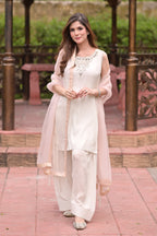 Woman in a white traditional outfit with a pink dupatta standing outdoors.