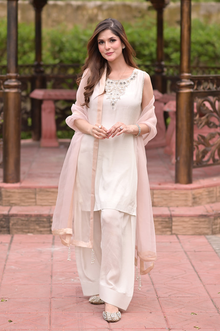 Woman in a white traditional outfit with a pink dupatta standing outdoors.