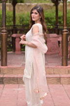 Woman in a light dress with a sheer pink overlay standing outdoors.