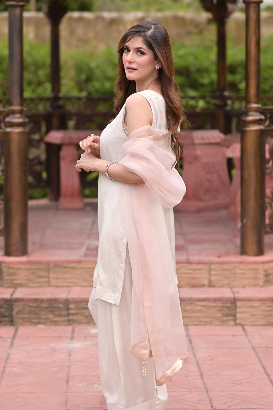 Woman in a light dress with a sheer pink overlay standing outdoors.