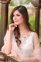 Woman in a white embroidered top with a sheer pink dupatta, sitting outdoors.