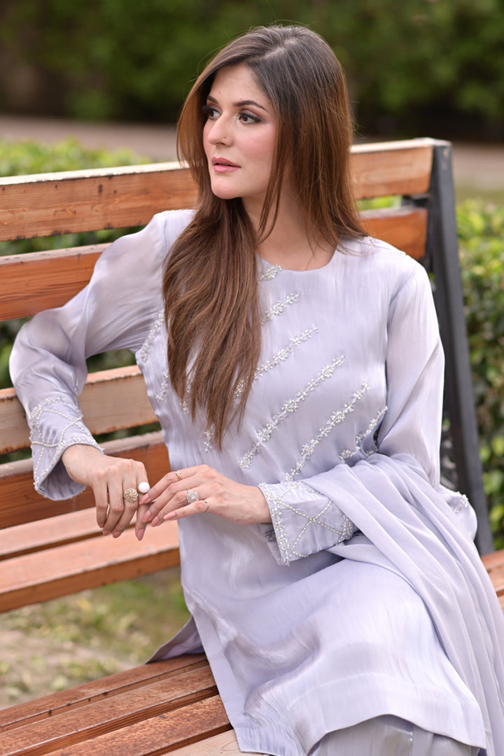 Woman in a light blue traditional outfit sitting on a wooden bench outdoors.