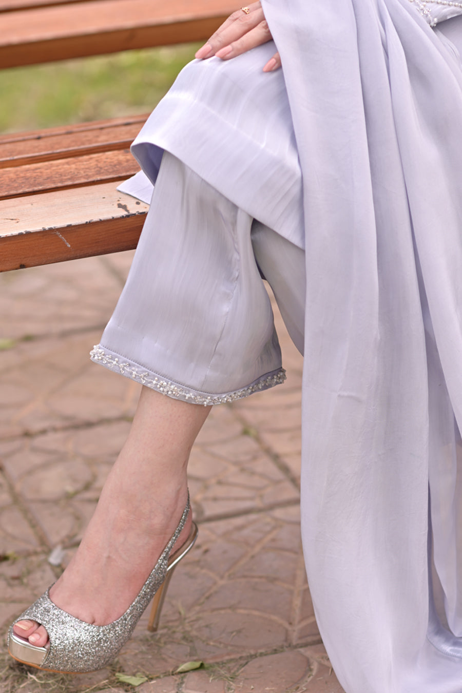 Person wearing a light gray dress with silver shoes on a stone path.