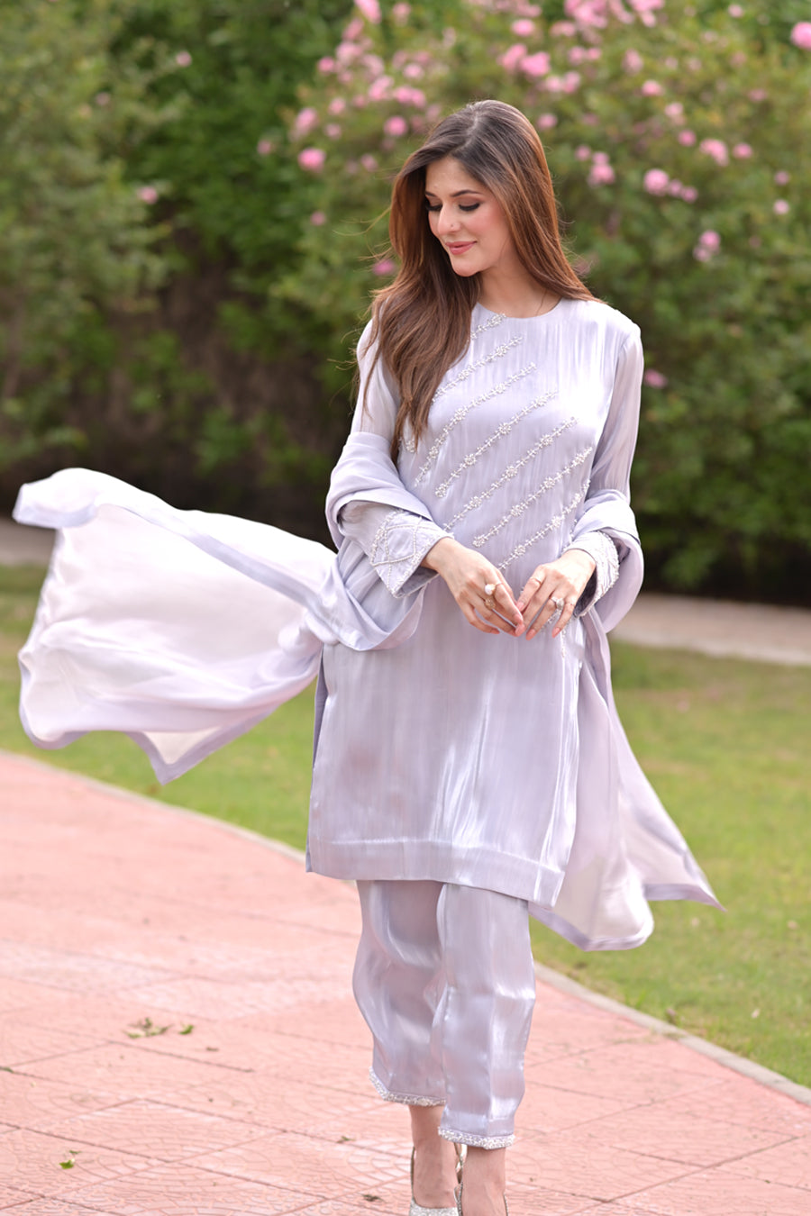 Woman in a light gray traditional outfit with a flowing fabric in an outdoor setting.