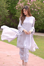 Woman in a light gray traditional outfit with a flowing fabric in an outdoor setting.