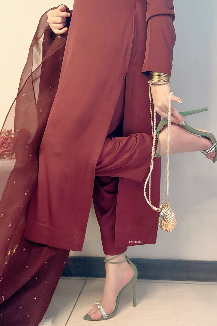 Person wearing a maroon outfit with high heels and a long sheer fabric.
