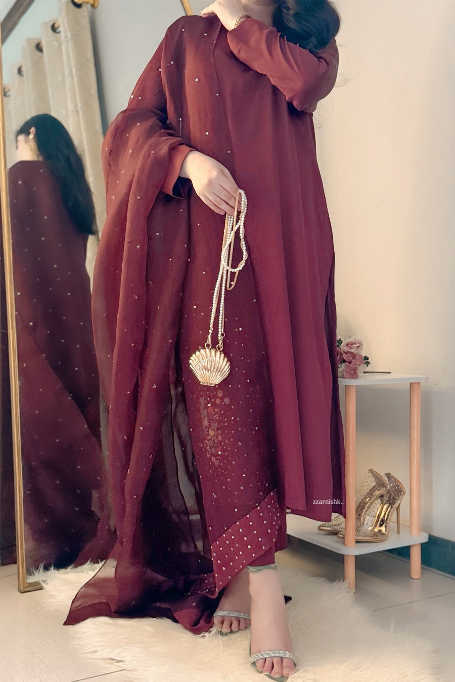 Person wearing a burgundy dress with gold accents in a room.