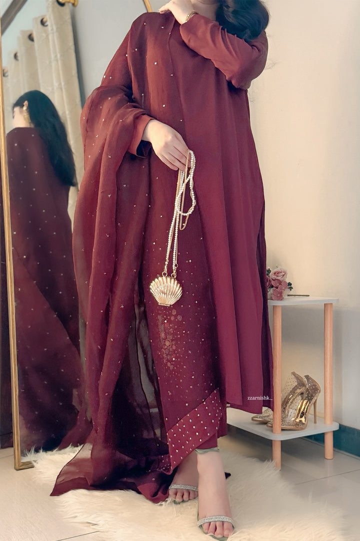 Person wearing a burgundy dress with gold accents in a room.