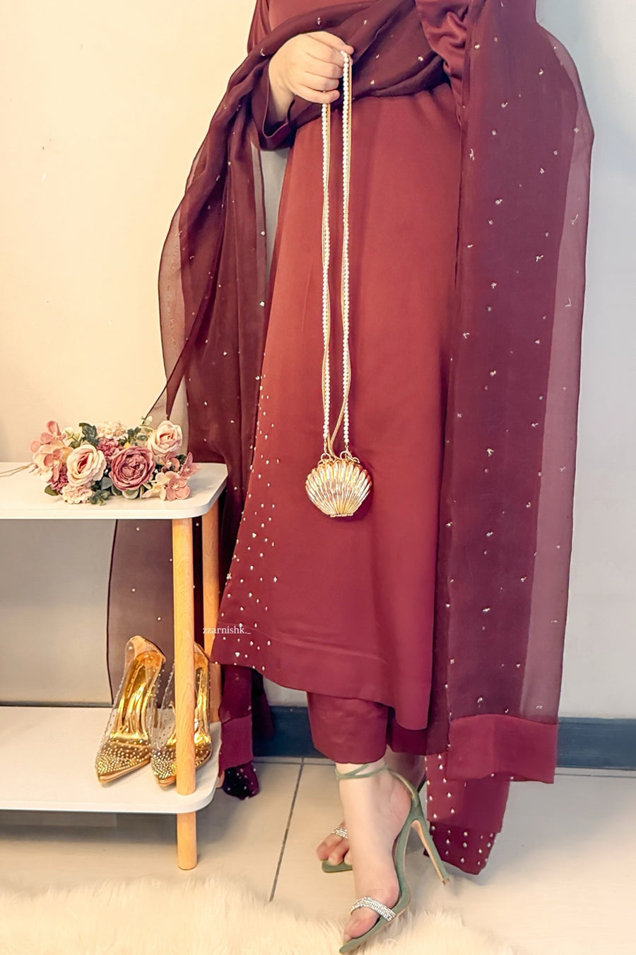 Person wearing a burgundy outfit with a matching scarf, holding a shell-shaped handbag.