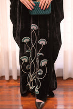 Person wearing a black outfit with floral embroidery, holding a green clutch.