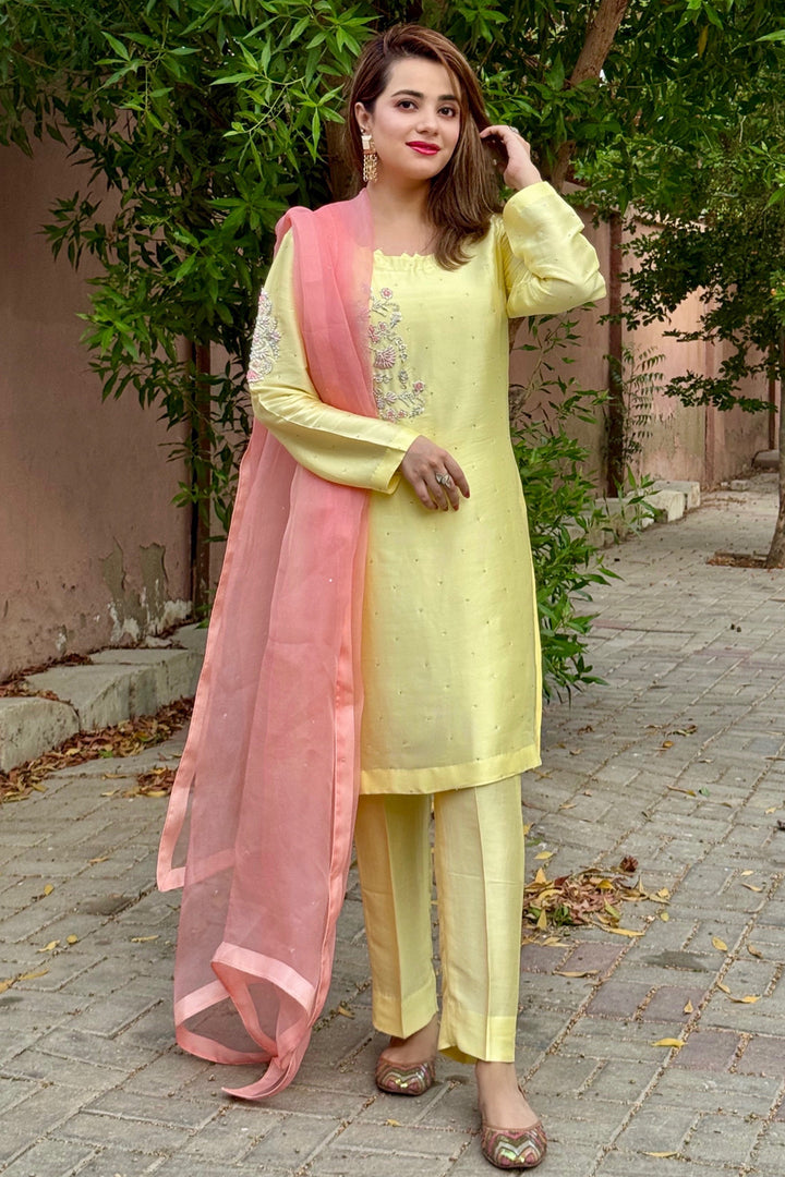 Woman in a light yellow outfit with a pink dupatta standing outdoors.