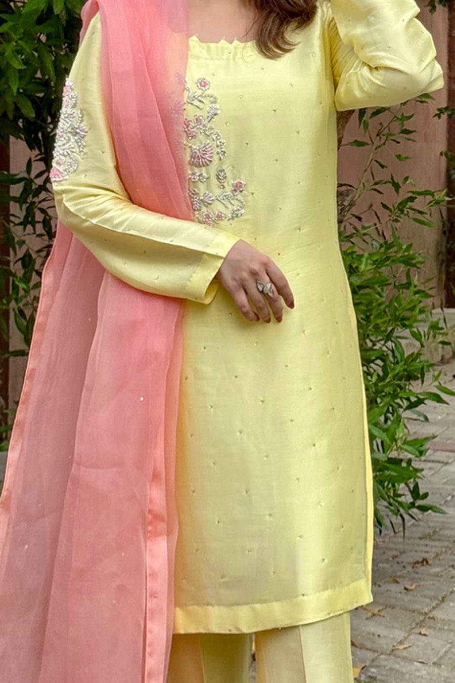 Woman wearing a light yellow embroidered kurta with pink dupatta against a natural background