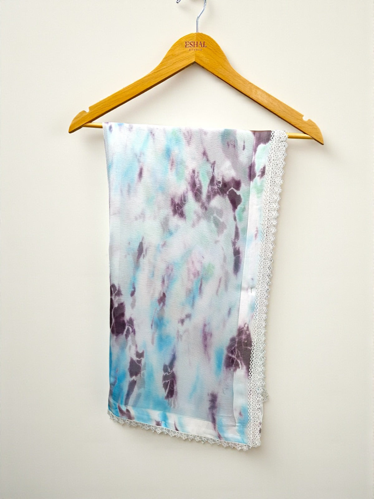 Scarf with tie-dye pattern and lace edge on a hanger against a white background