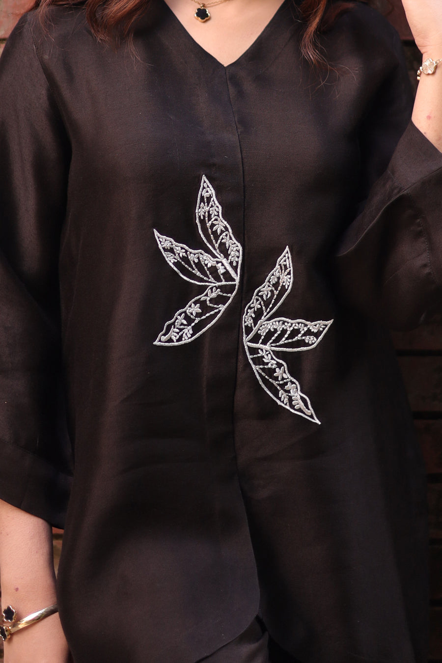 Black garment with white leaf embroidery on a dark background