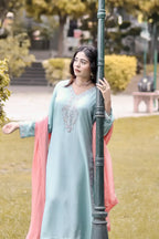 Woman in a light blue traditional outfit with pink dupatta standing outdoors.