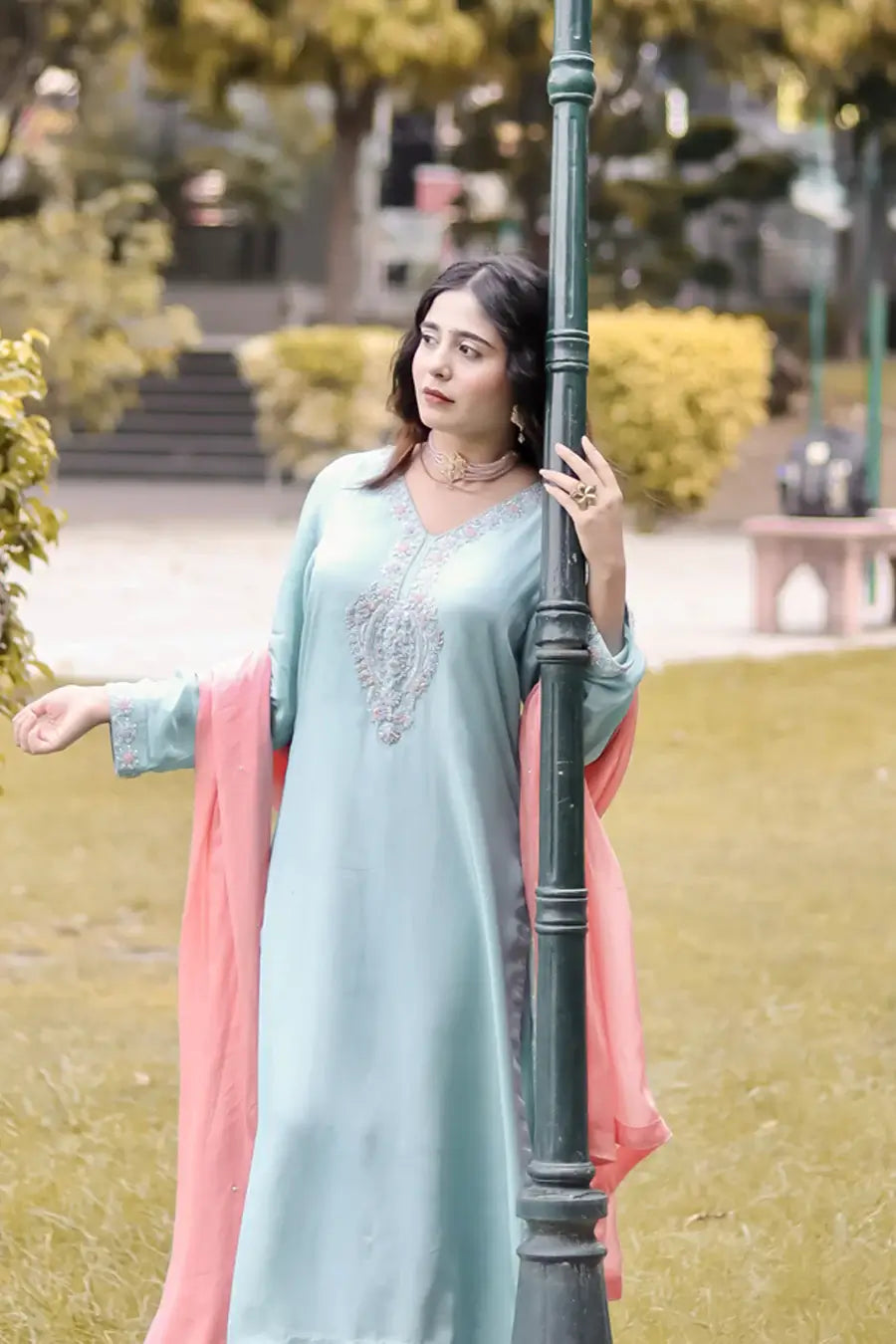 Woman in a light blue traditional outfit with pink dupatta standing outdoors.
