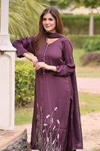 Woman wearing a purple dress with floral embroidery in an outdoor setting