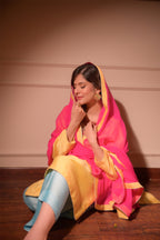 Woman in a pink and yellow traditional outfit sitting on the floor against a beige wall.