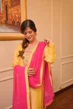 Woman in a yellow and pink traditional outfit indoors with a decorative wall in the background