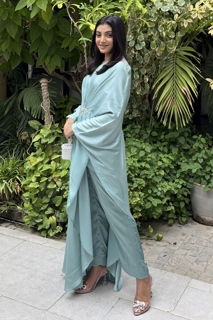 Woman in a light blue traditional outfit standing in front of green plants.