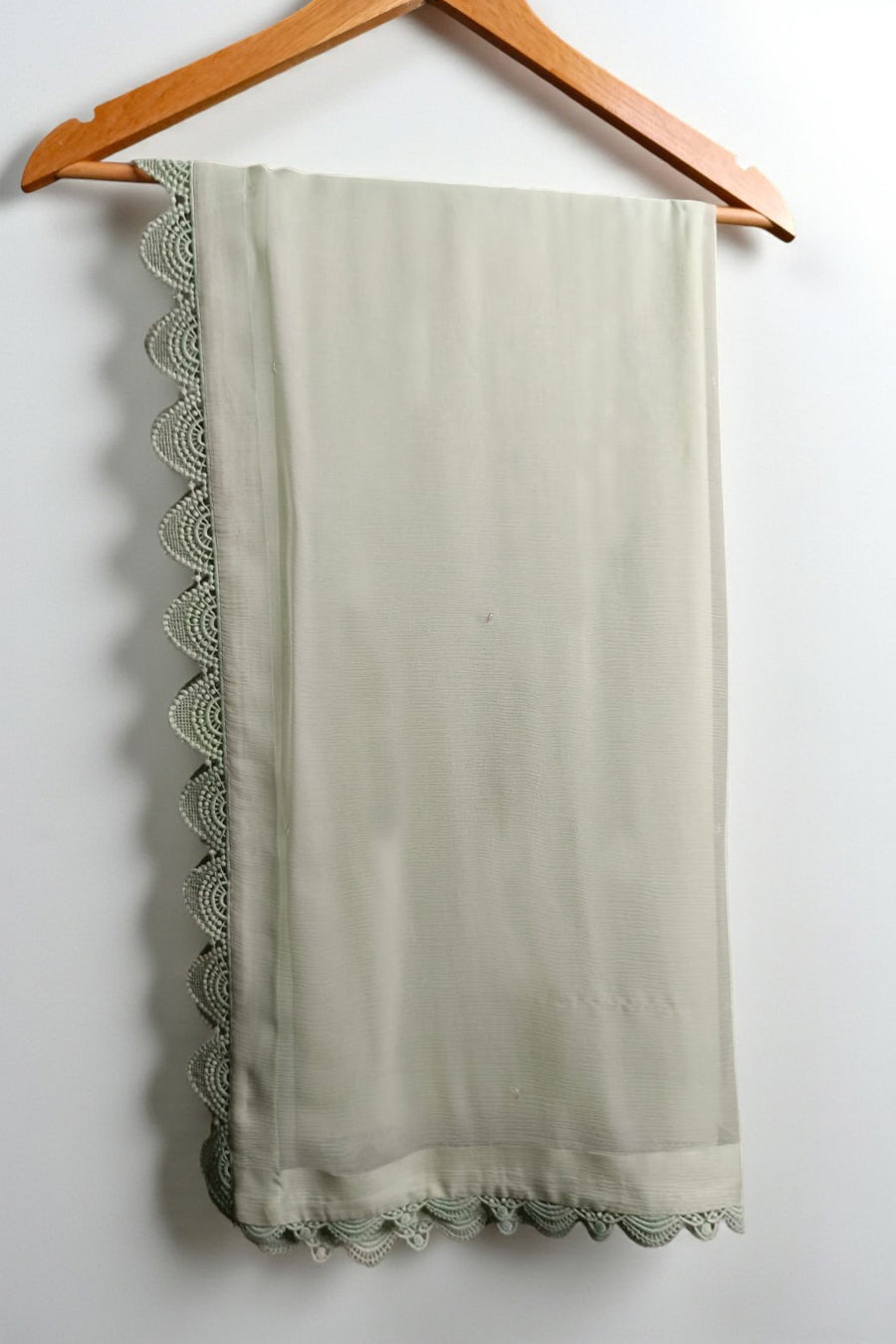 Light green scarf with lace trim hanging on a wooden hanger against a white background