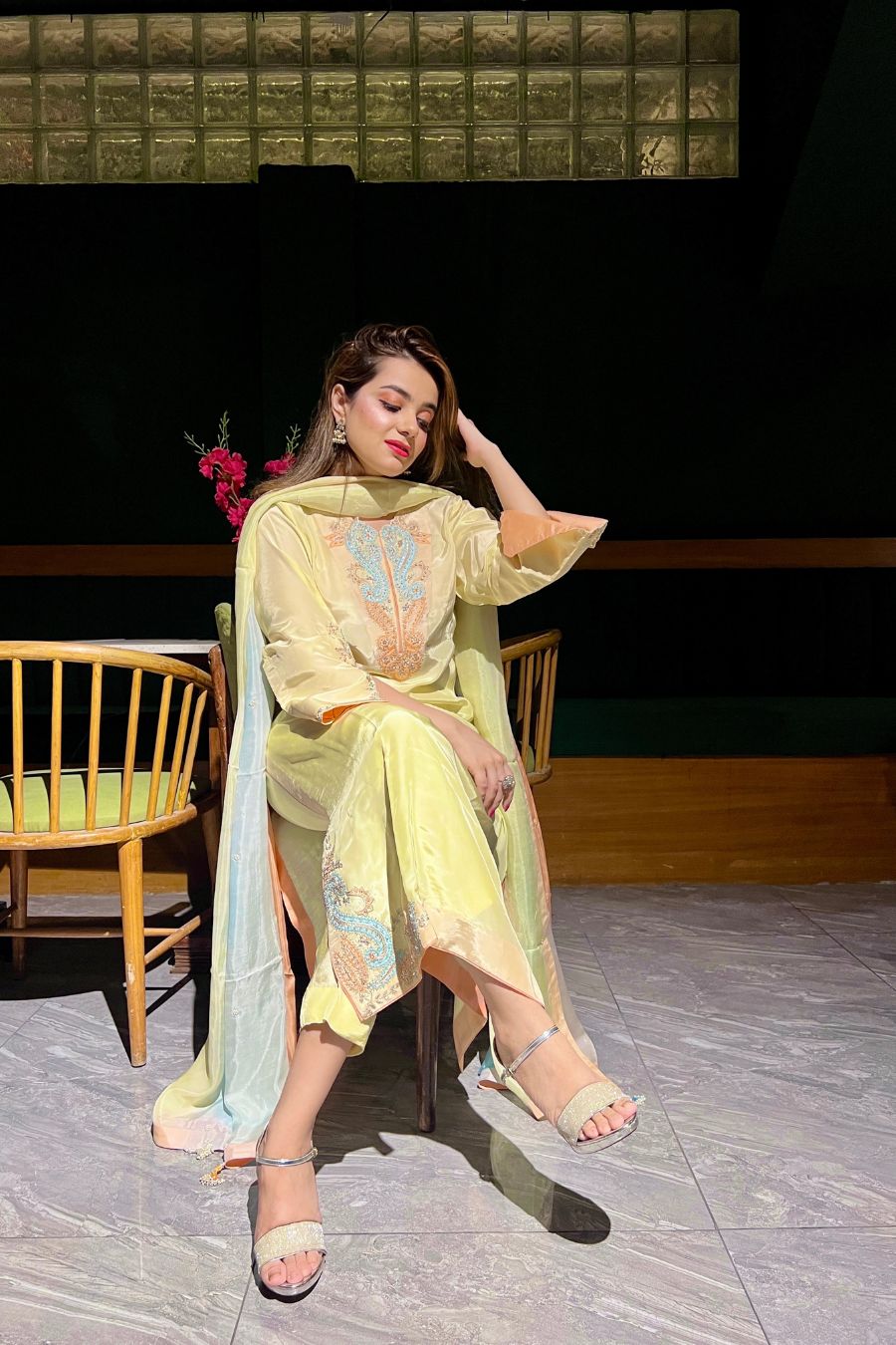 Woman in a light yellow traditional outfit sitting on a chair with a dark background