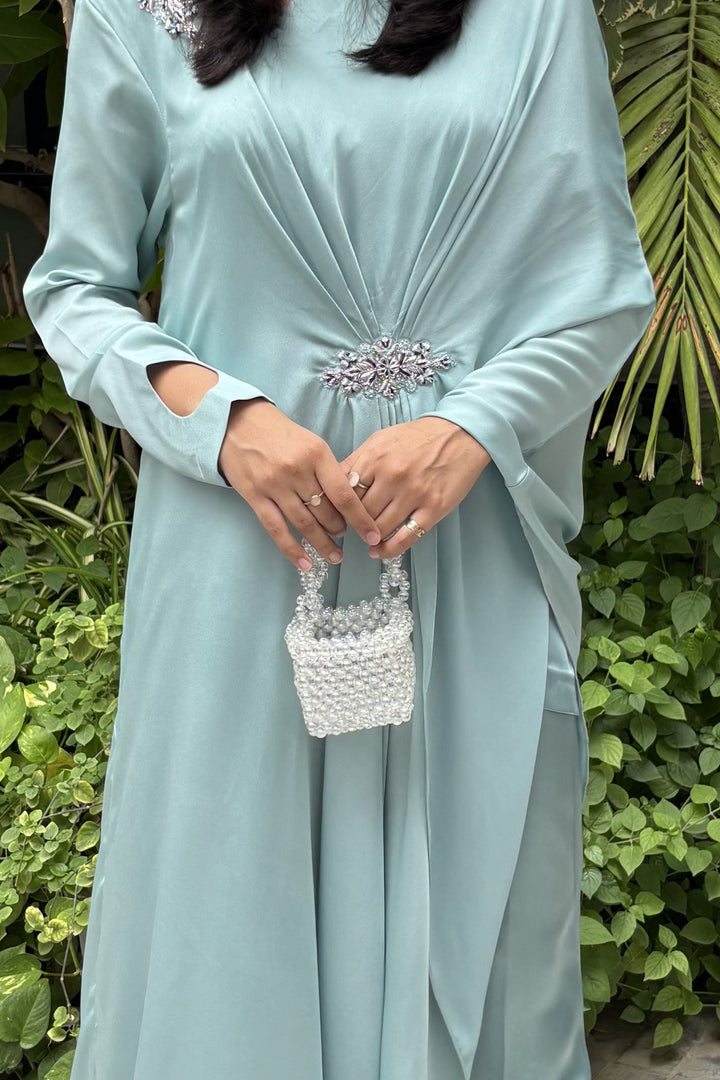 Woman in a light blue dress holding a small decorative basket against a green leafy background